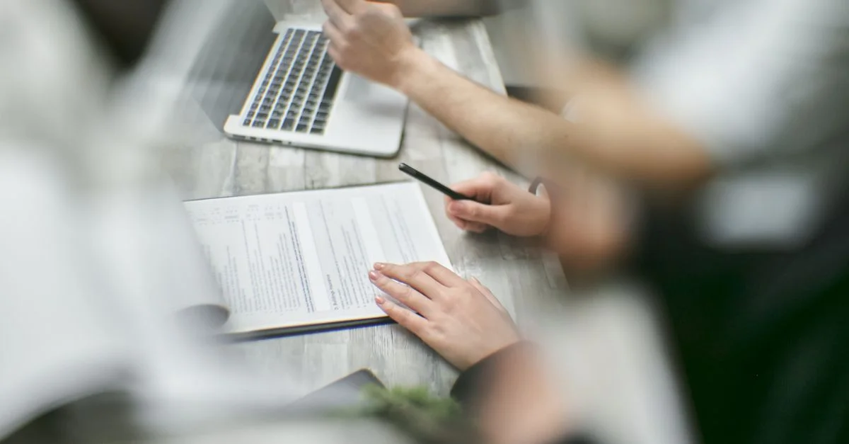 Vista en primer plano de un equipo colaborando con documentos y un portátil en un entorno de oficina.
