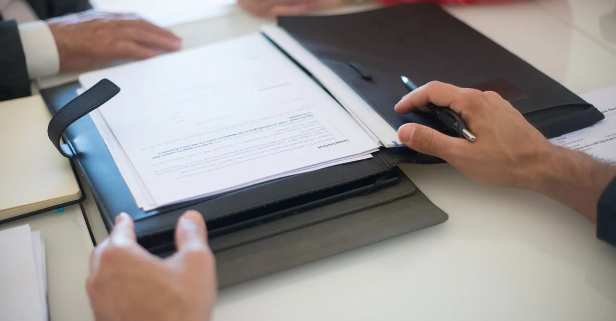 Dos profesionales discutiendo un contrato con documentos sobre una mesa, en interiores.