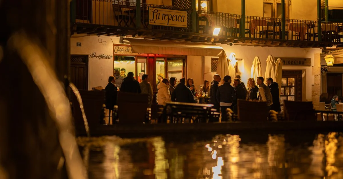 Una animada escena nocturna en un restaurante de Chinchón, España, donde un grupo de personas disfruta de una cálida velada.
