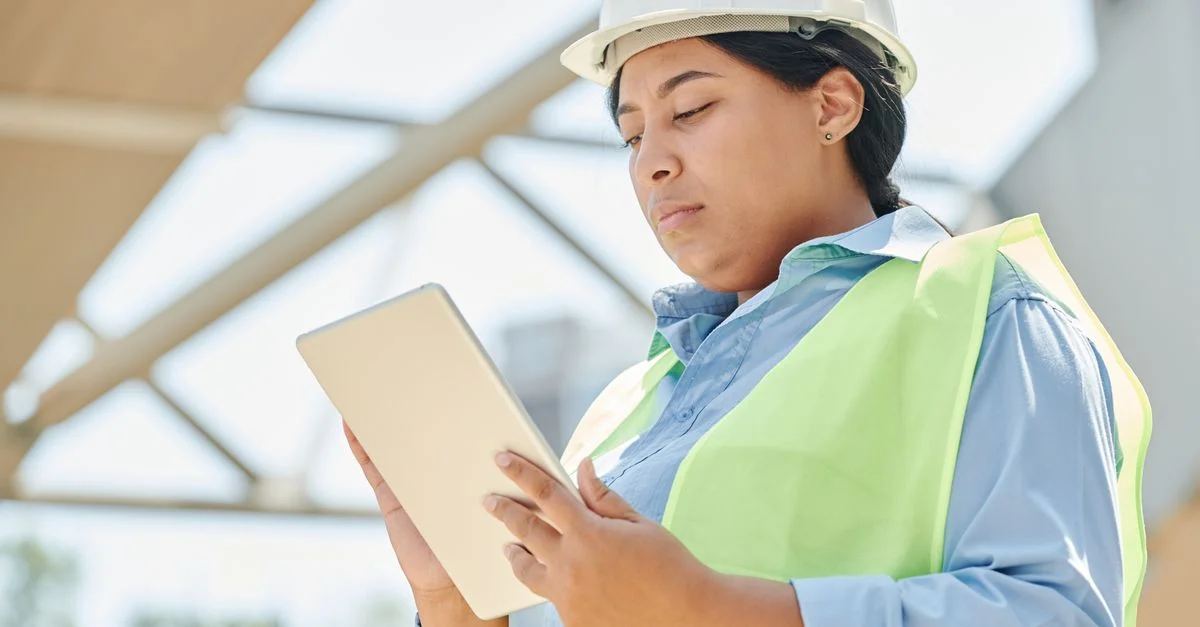 Ingeniera femenina confiada con casco usando una tableta en una obra de construcción al aire libre.