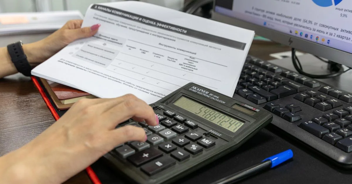 Una persona calcula datos financieros usando una calculadora y un documento, trabajando en un escritorio de oficina.