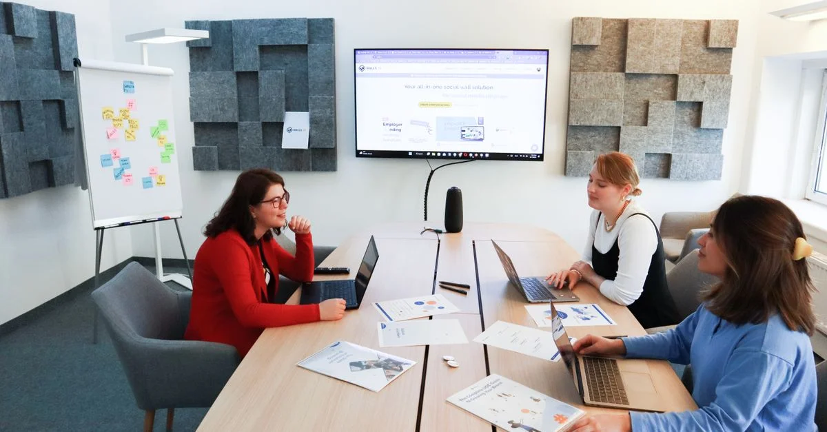 Tres mujeres participando en una reunión de negocios discutiendo ideas con portátiles y documentos en un entorno de oficina moderno.