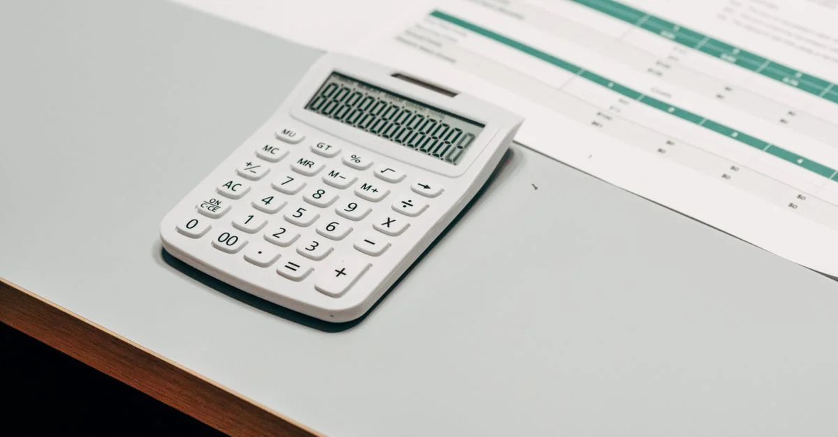 Close-up de una calculadora blanca junto a una hoja de cálculo financiera en un escritorio.