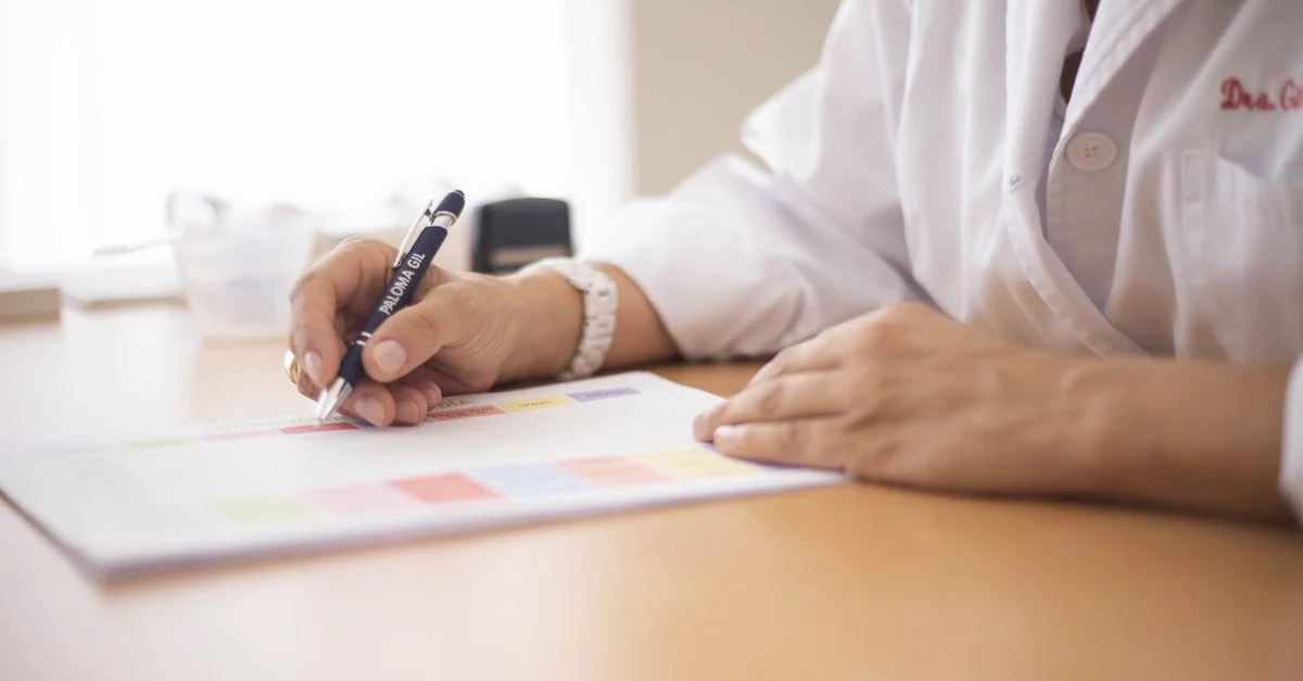 Primer plano de una doctora escribiendo una receta en un escritorio en un entorno de oficina.