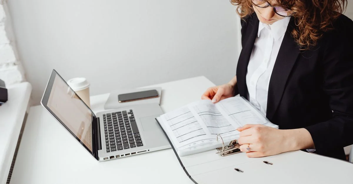 Mujer de negocios leyendo documentos en una laptop en un entorno de oficina en casa. Ideal para temas de trabajo desde casa.
