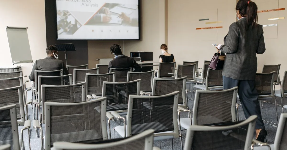 Configuración de la sala de conferencias para un seminario empresarial, con asistentes usando mascarillas.