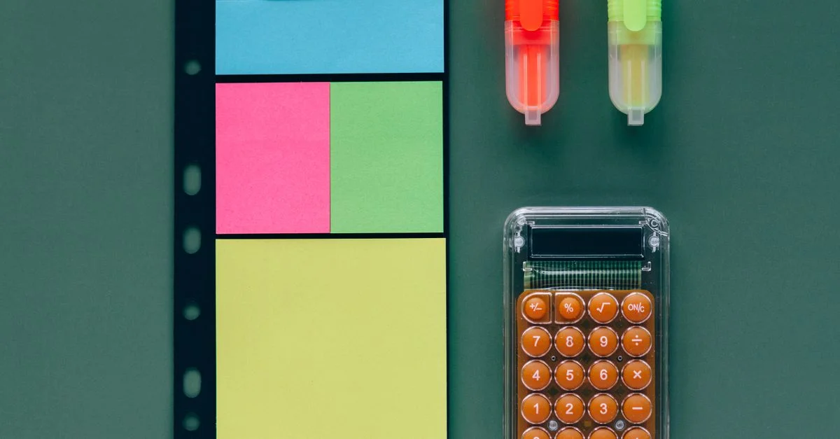 Plano cenital de útiles de oficina coloridos, incluyendo calculadora, notas adhesivas y resaltadores.