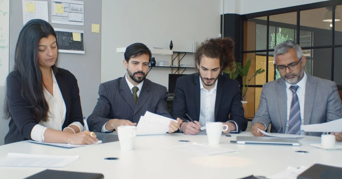 Grupo de profesionales de negocios participando en una reunión de equipo alrededor de un escritorio en un entorno de oficina moderna.