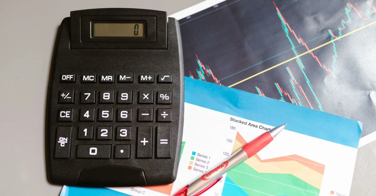 Calculadora y bolígrafo en un escritorio con gráficos financieros, mostrando análisis y planificación empresarial.
