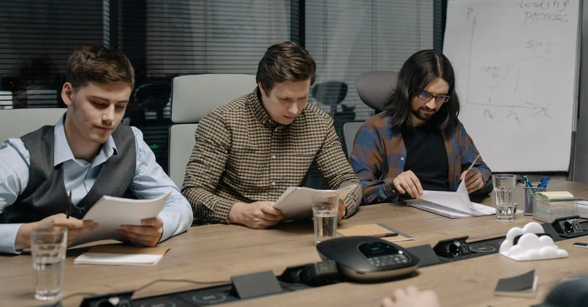 Tres colegas de negocios revisando documentos en una sala de conferencias moderna durante una reunión diurna.